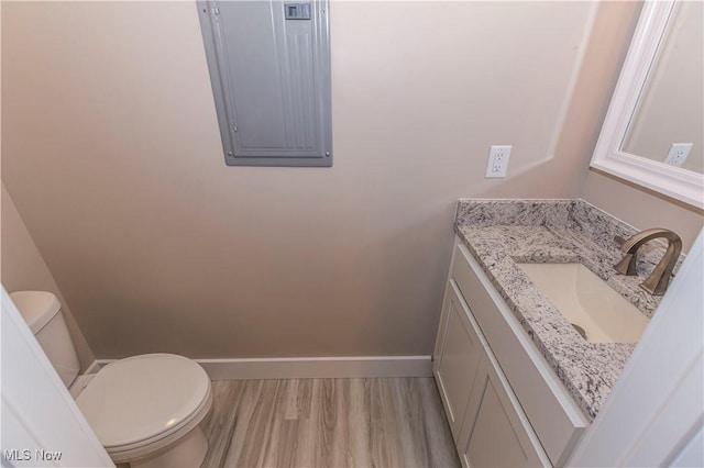 half bath with electric panel, wood finished floors, vanity, baseboards, and toilet