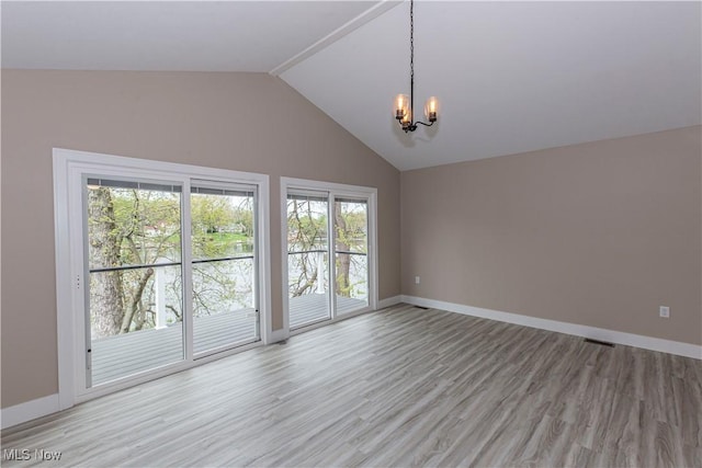 empty room with an inviting chandelier, light wood-style floors, a wealth of natural light, and vaulted ceiling