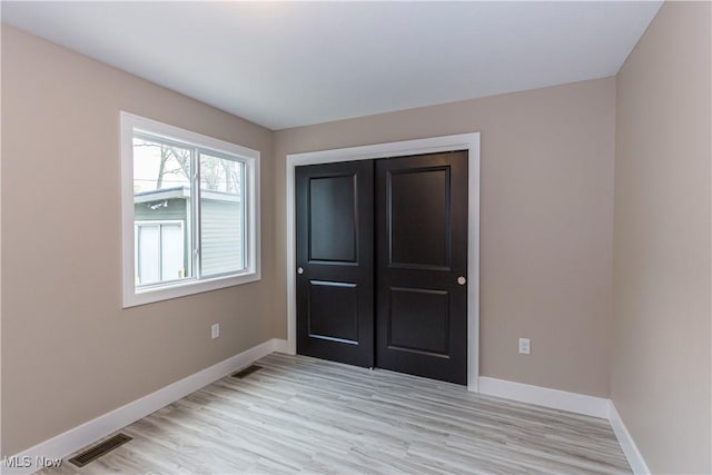 unfurnished bedroom featuring baseboards, a closet, light wood-style flooring, and visible vents