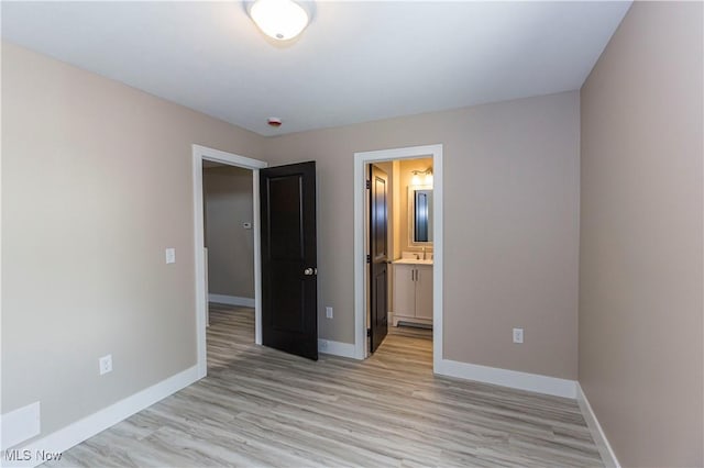 unfurnished bedroom featuring light wood-style floors, baseboards, ensuite bathroom, and a sink