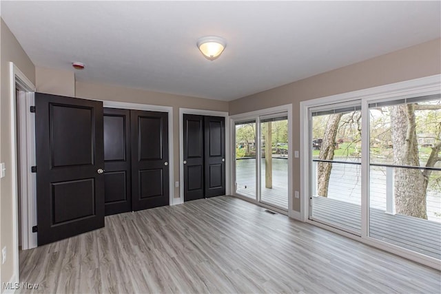 unfurnished bedroom with light wood-style floors, multiple closets, access to exterior, baseboards, and visible vents