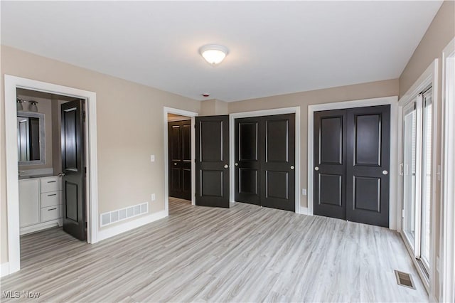 unfurnished bedroom featuring two closets, baseboards, visible vents, and light wood-style flooring