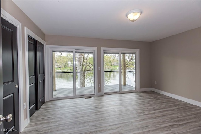 empty room featuring light wood-style floors, baseboards, a water view, and visible vents