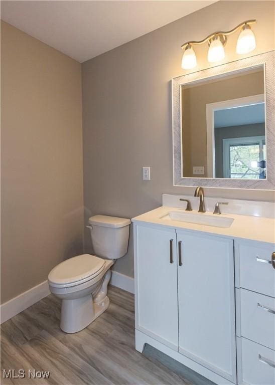 half bath featuring baseboards, vanity, toilet, and wood finished floors