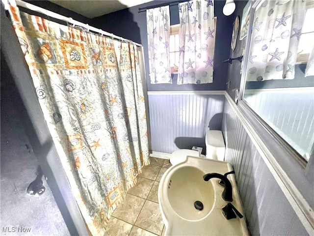 full bathroom featuring tile patterned flooring, a wainscoted wall, and curtained shower
