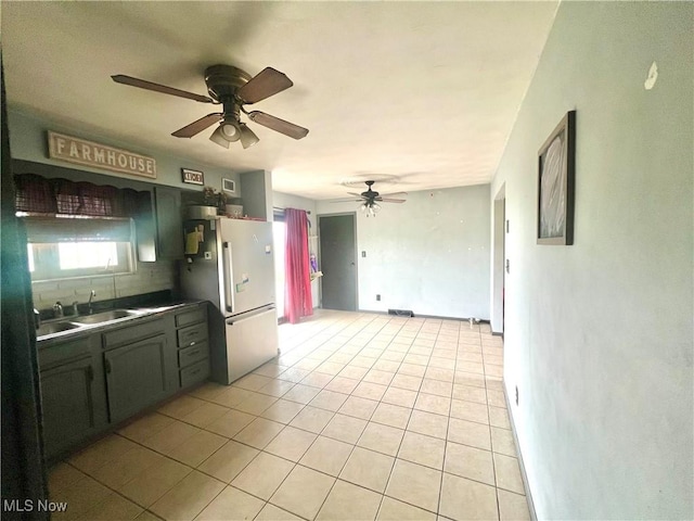 kitchen with freestanding refrigerator, light tile patterned flooring, dark countertops, ceiling fan, and a sink