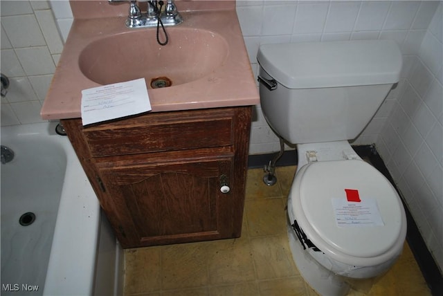 bathroom featuring a bath, vanity, toilet, and tile walls