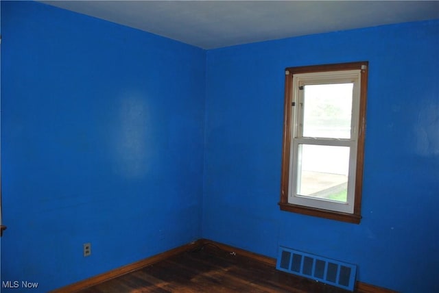 empty room featuring dark wood-style flooring, baseboards, visible vents, and a healthy amount of sunlight
