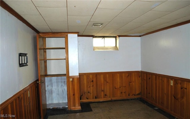 basement with wooden walls, ornamental molding, and a wainscoted wall
