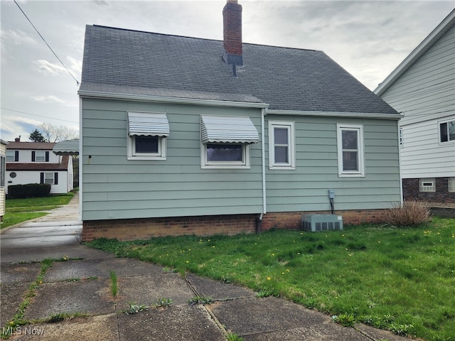rear view of house with a yard, a chimney, a shingled roof, and central AC unit