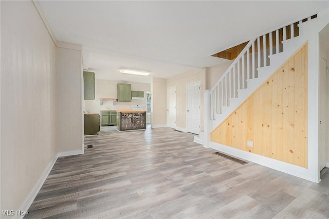 unfurnished living room featuring baseboards, stairs, wood finished floors, and visible vents