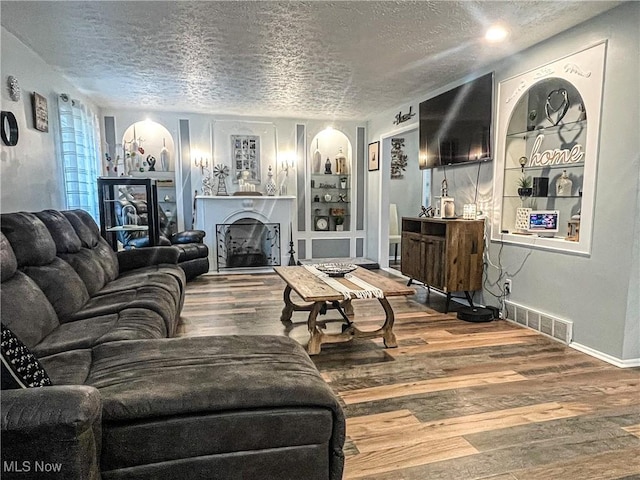 living room with visible vents, wood finished floors, a fireplace, a textured ceiling, and arched walkways