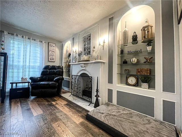 living area featuring a textured ceiling, built in shelves, wood finished floors, and a fireplace