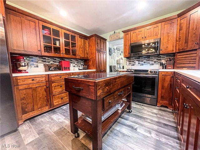 kitchen with backsplash, appliances with stainless steel finishes, glass insert cabinets, and light wood-style floors
