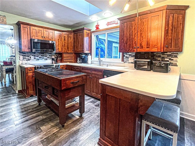 kitchen with backsplash, a kitchen bar, a sink, stainless steel microwave, and a peninsula