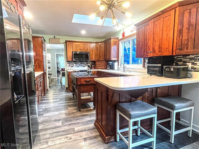 kitchen featuring appliances with stainless steel finishes, a sink, a peninsula, wood finished floors, and backsplash