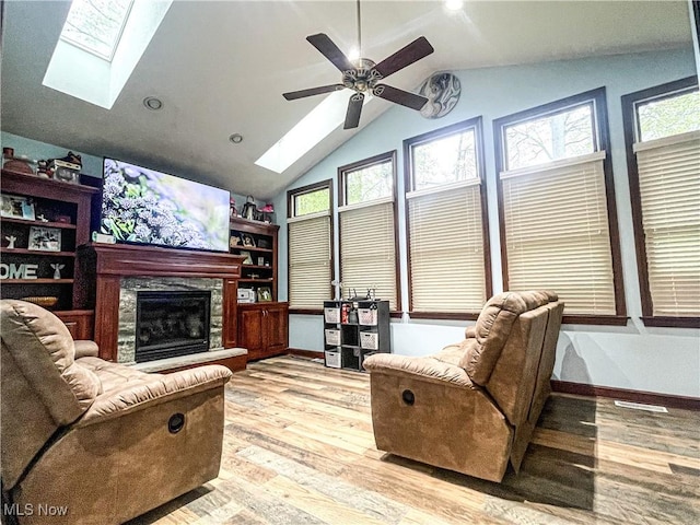 living room with ceiling fan, a glass covered fireplace, wood finished floors, and vaulted ceiling with skylight