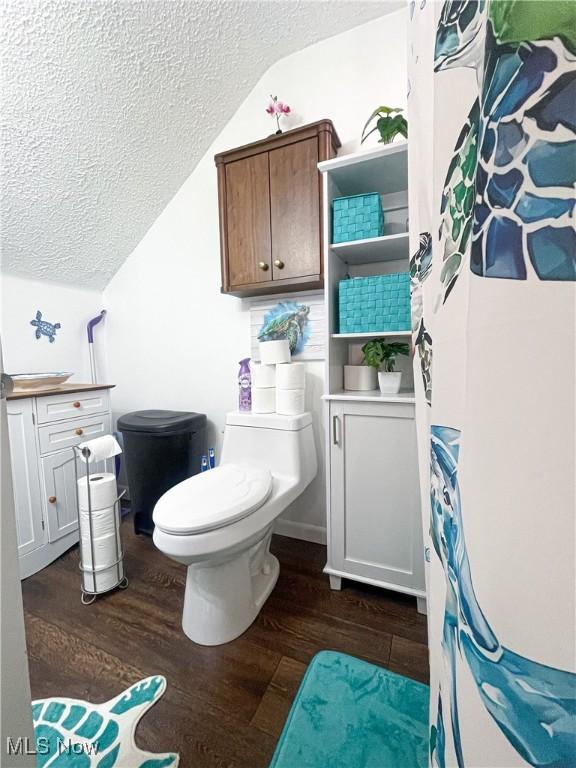 bathroom featuring a textured ceiling, lofted ceiling, wood finished floors, and toilet