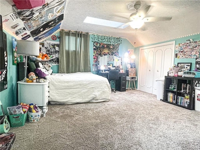 bedroom featuring a closet, vaulted ceiling with skylight, a textured ceiling, ceiling fan, and carpet floors