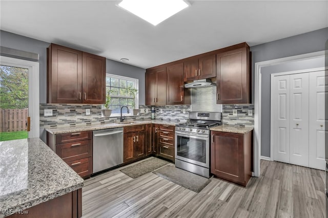 kitchen with a sink, appliances with stainless steel finishes, under cabinet range hood, and light wood-type flooring