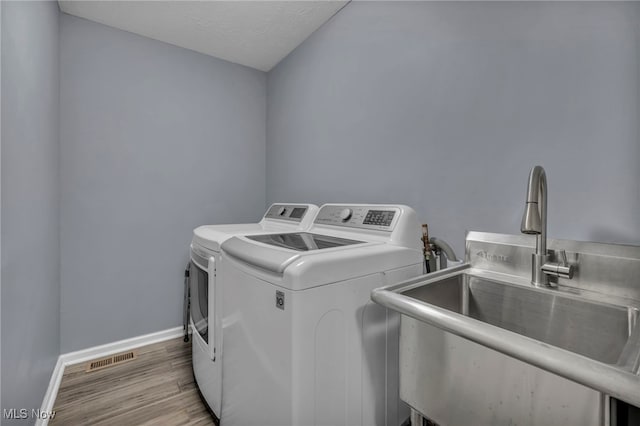 clothes washing area with laundry area, visible vents, wood finished floors, washer and clothes dryer, and a sink