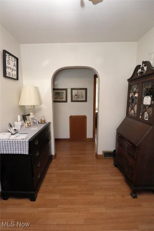 hall with arched walkways, baseboards, light wood-style flooring, and visible vents