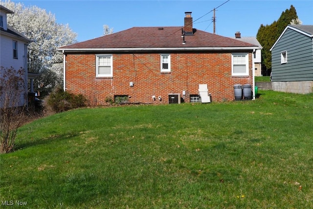 rear view of house featuring a yard, brick siding, cooling unit, and a chimney