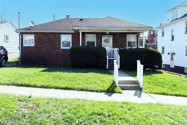 bungalow with brick siding, a shingled roof, and a front yard