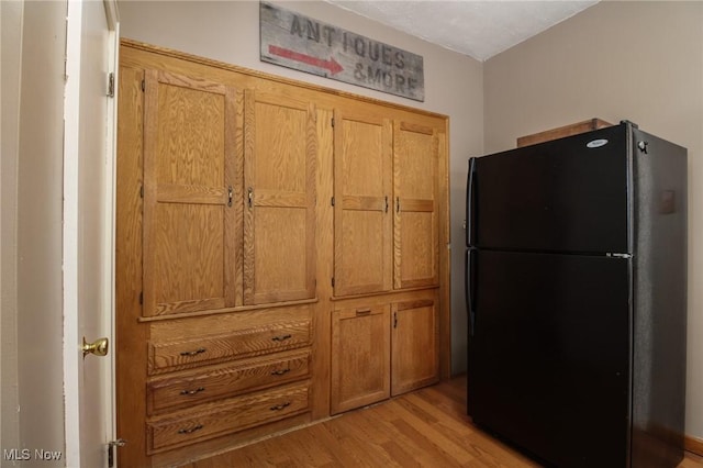 interior space featuring freestanding refrigerator, brown cabinetry, and light wood-style flooring