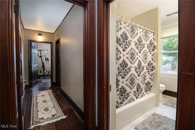 bathroom featuring toilet, shower / bath combo with shower curtain, baseboards, wood finished floors, and visible vents