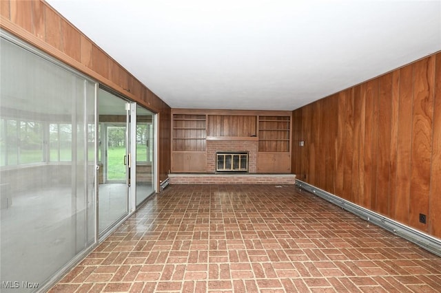 unfurnished living room with wooden walls, brick patterned floor, a fireplace, and built in shelves