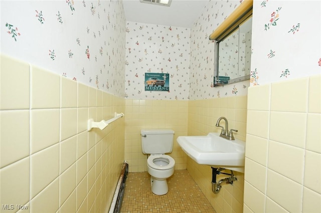 half bath featuring baseboard heating, wallpapered walls, toilet, tile patterned flooring, and a wainscoted wall