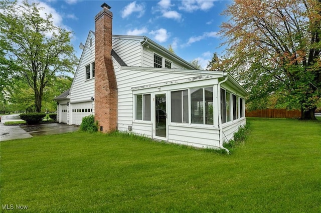 view of side of property with a chimney, driveway, fence, an attached garage, and a sunroom