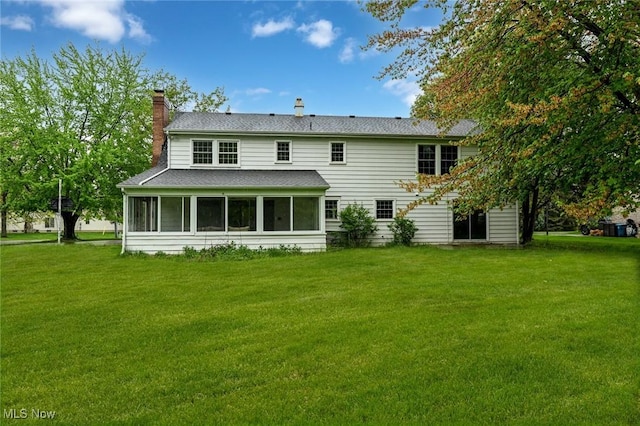 rear view of property with a yard, roof with shingles, a sunroom, and a chimney