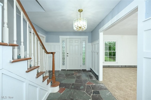 carpeted foyer entrance with stairs, stone finish floor, and a notable chandelier