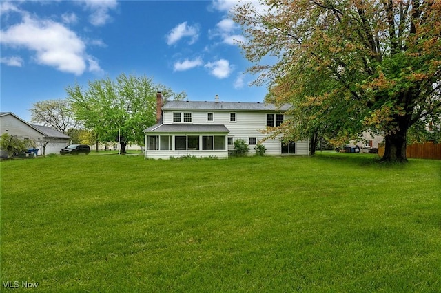 rear view of house featuring a chimney, a yard, and a sunroom