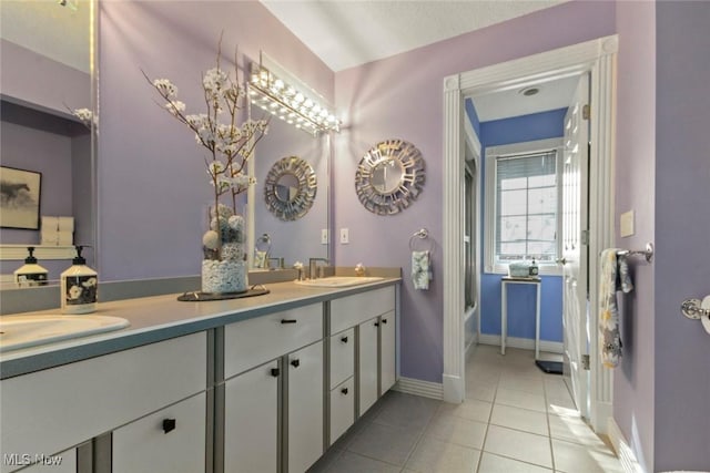 full bath with a sink, a bathtub, tile patterned floors, double vanity, and baseboards