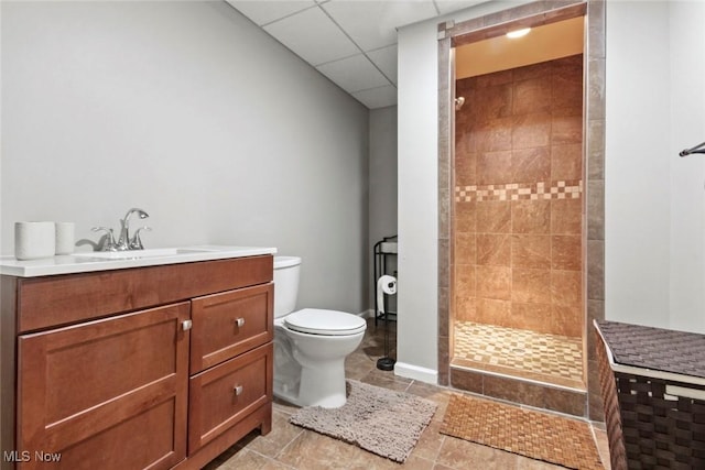 full bathroom featuring baseboards, toilet, a tile shower, vanity, and a paneled ceiling