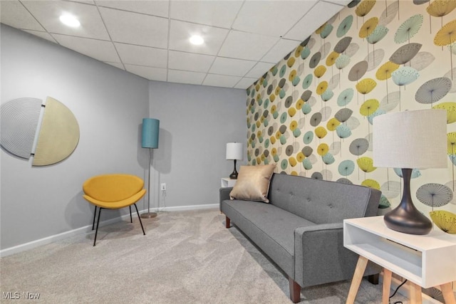 living area with a drop ceiling, wallpapered walls, carpet floors, baseboards, and an accent wall