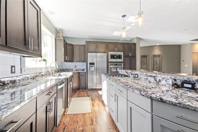 kitchen featuring hanging light fixtures, light wood-style floors, stainless steel appliances, and light stone counters