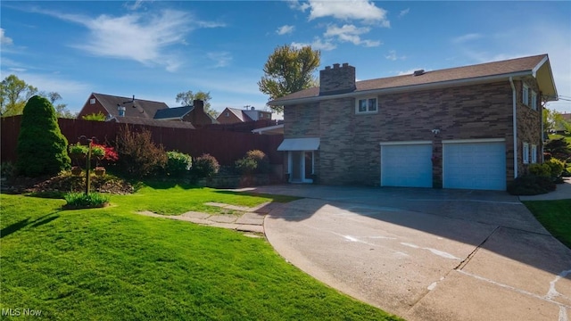 back of property with an attached garage, fence, a chimney, a lawn, and driveway