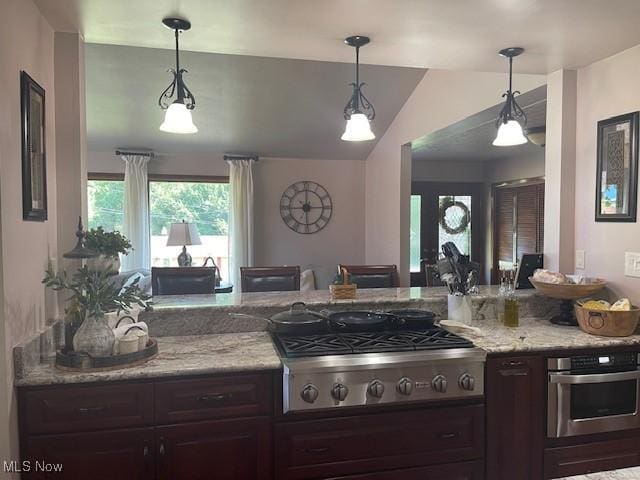 kitchen featuring pendant lighting, dark brown cabinets, light stone counters, vaulted ceiling, and stainless steel appliances