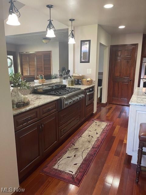 kitchen featuring stainless steel appliances, decorative light fixtures, light stone counters, dark wood-type flooring, and recessed lighting
