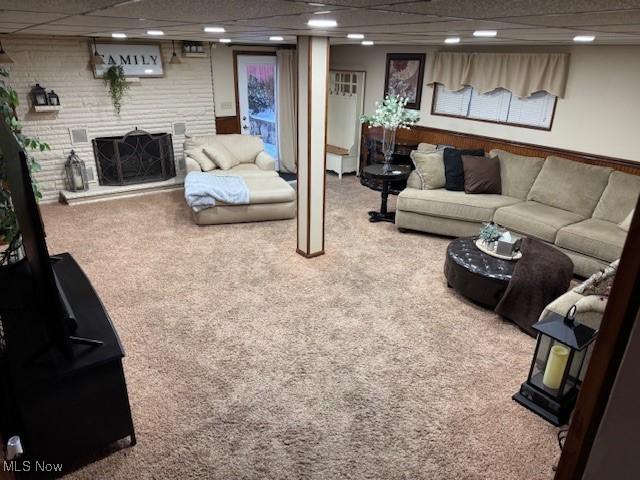 carpeted living room featuring a drop ceiling and a brick fireplace
