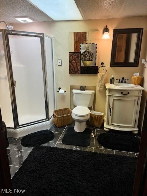 bathroom with a shower stall, vanity, toilet, and a textured ceiling