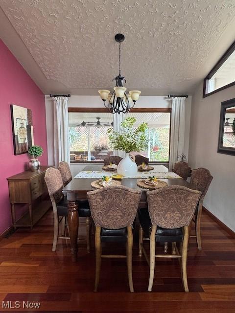 dining space featuring a textured ceiling, vaulted ceiling, wood finished floors, and a notable chandelier
