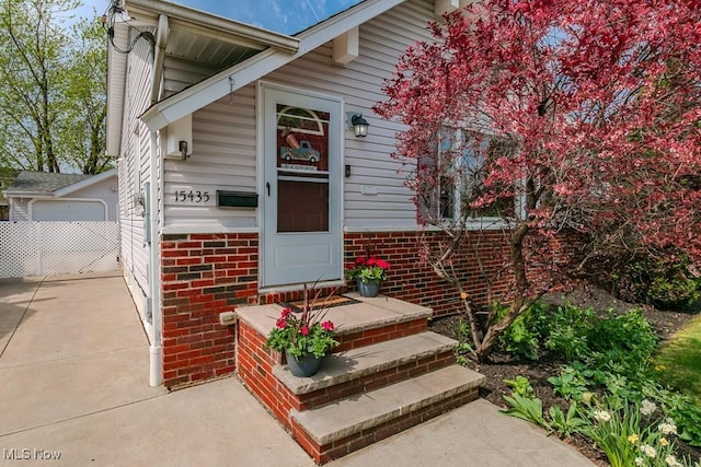 property entrance with concrete driveway, brick siding, fence, and a detached garage