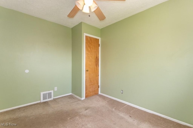 carpeted empty room with baseboards, ceiling fan, visible vents, and a textured ceiling