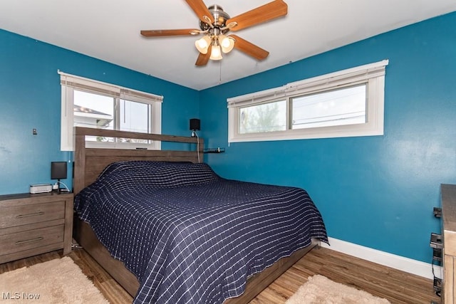 bedroom with baseboards, multiple windows, ceiling fan, and wood finished floors
