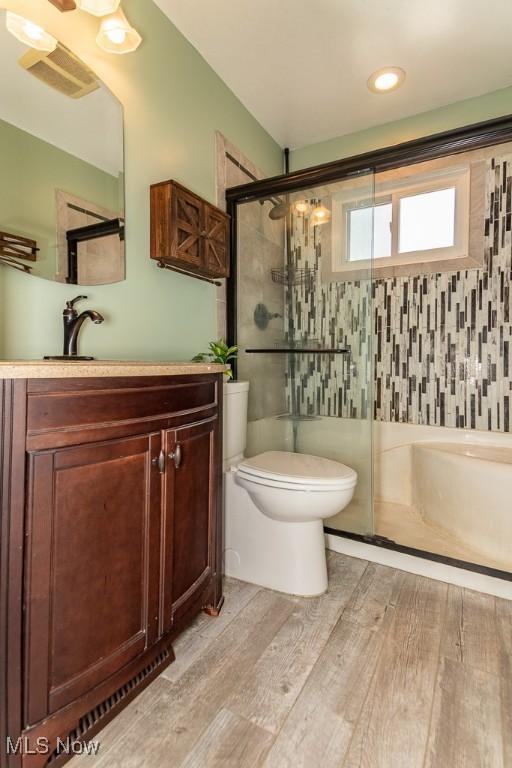 full bath featuring toilet, wood finished floors, a stall shower, visible vents, and vanity